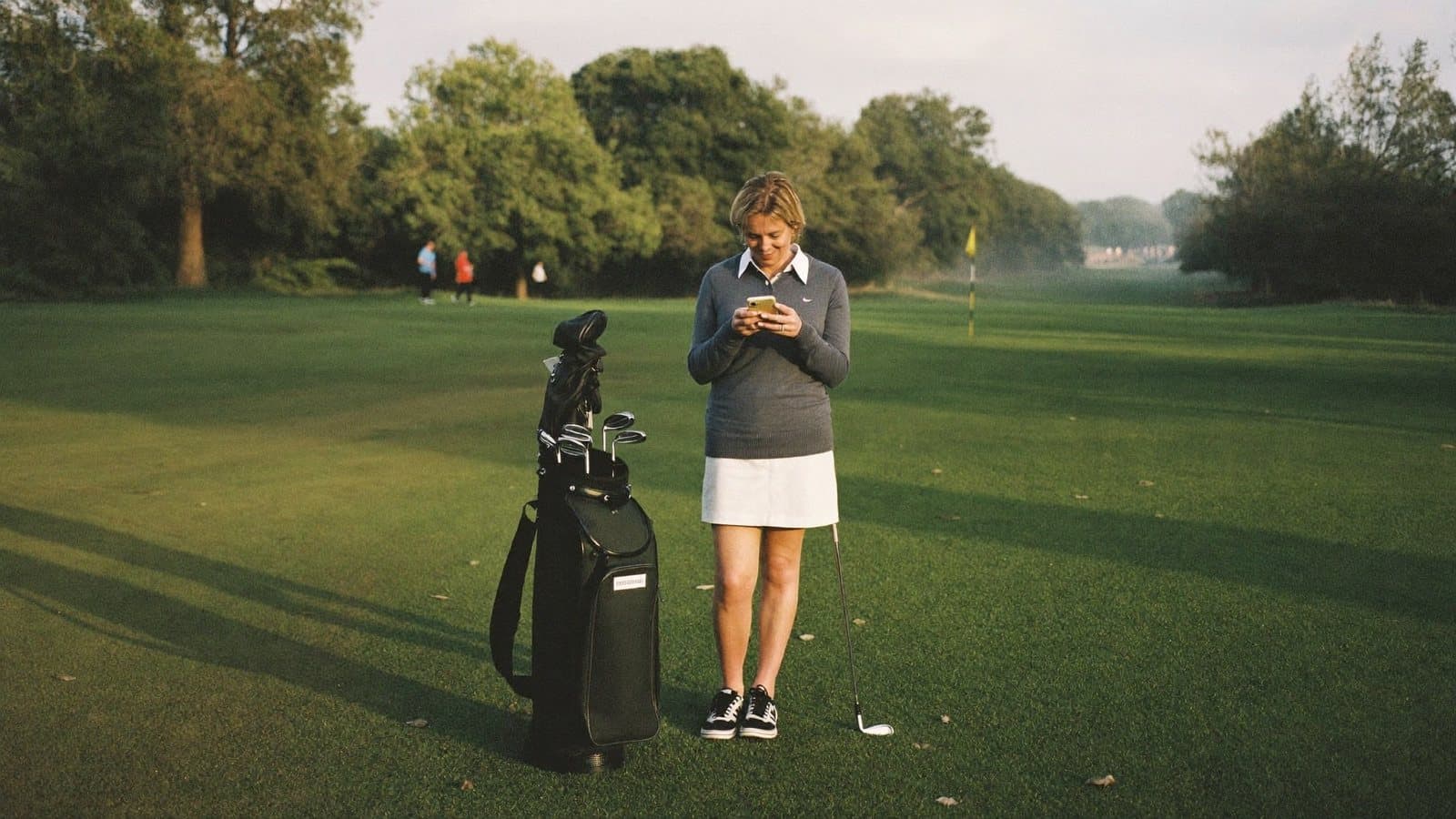 A golfer checking her phone on the fairway beside her bag